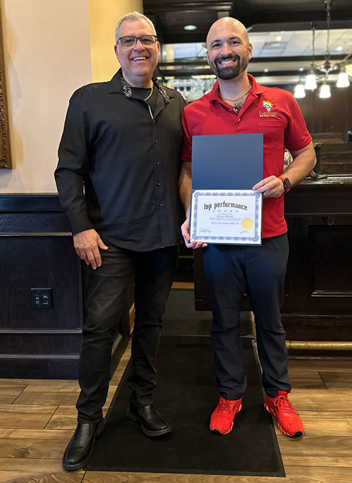 Photo of Al and award recipient smiling, holding a certificate of Outstanding Sales, standing in a restaurant or bar setting.