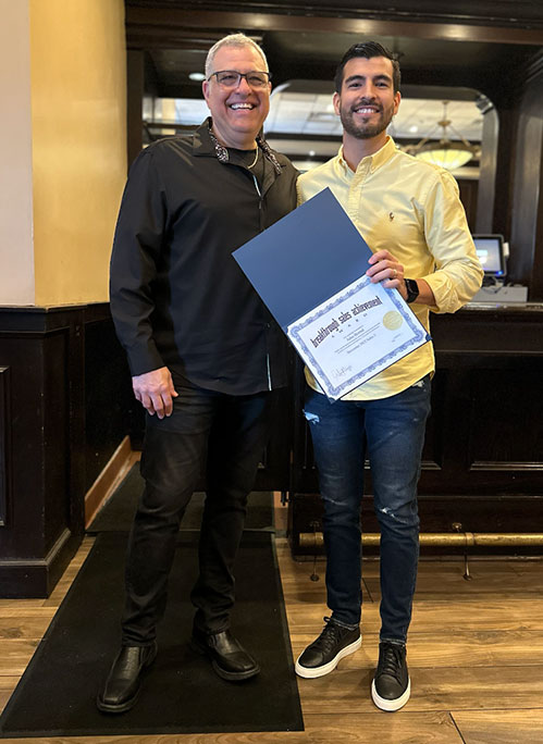 Photo of Al and award recipient smiling, holding a certificate of Outstanding Sales, standing in a restaurant or bar setting.
