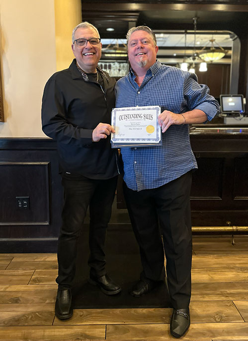 Photo of Al and award recipient smiling, holding a certificate of Outstanding Sales, standing in a restaurant or bar setting.