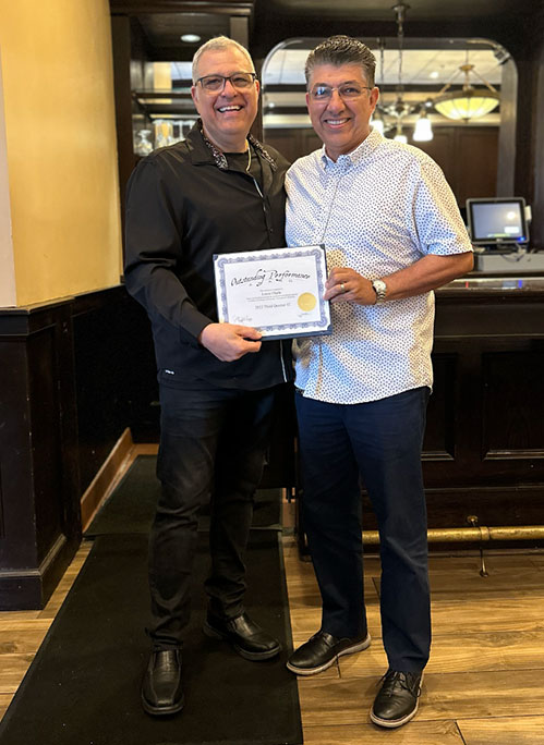 Photo of Al and award recipient smiling, holding a certificate of Outstanding Sales, standing in a restaurant or bar setting.