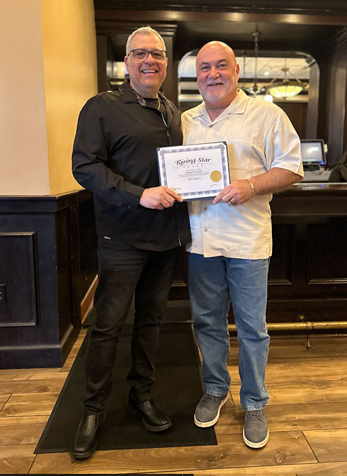 Photo of Al and award recipient smiling, holding a certificate of Outstanding Sales, standing in a restaurant or bar setting.