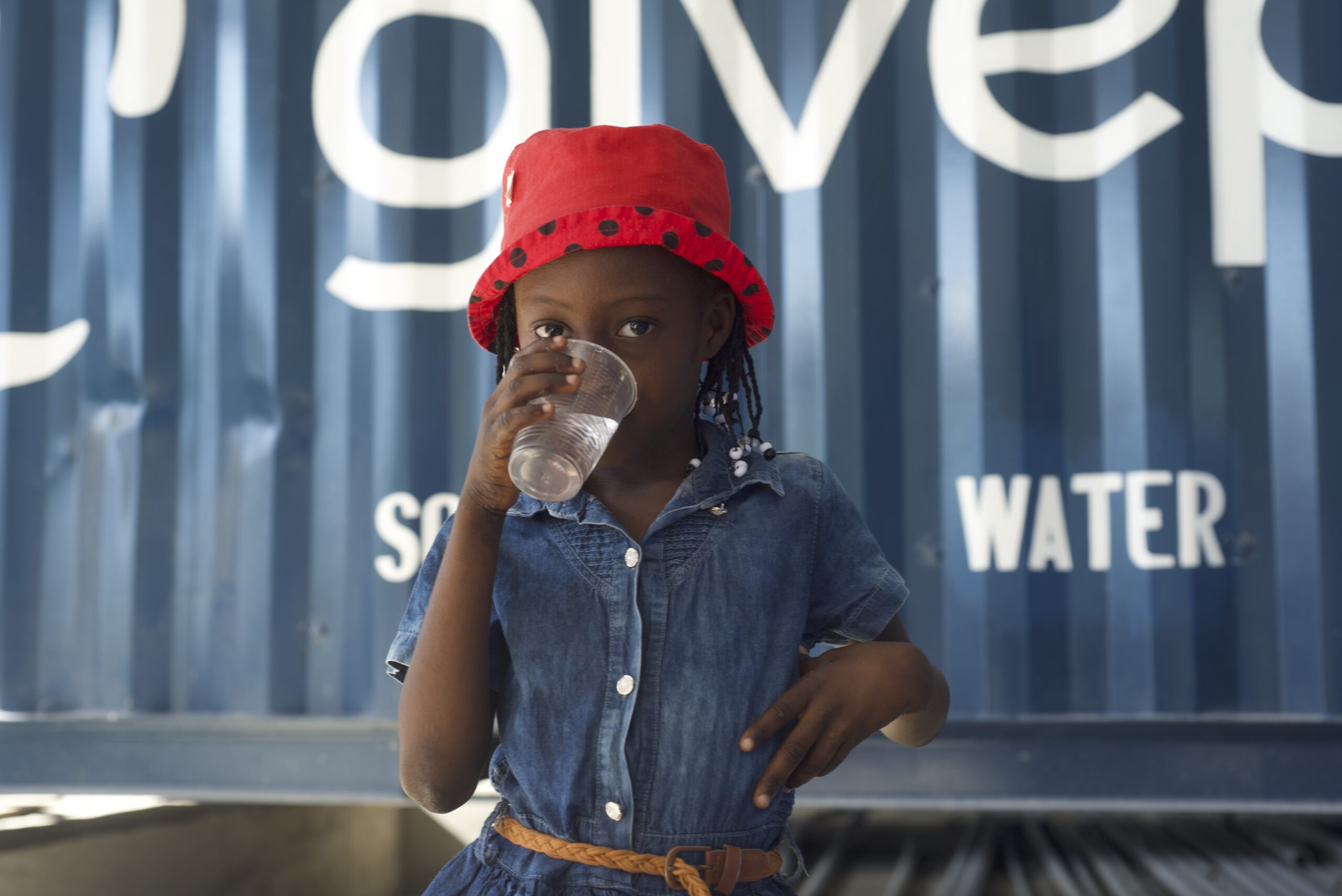 Young girl drinking water in front of a GivePower container.